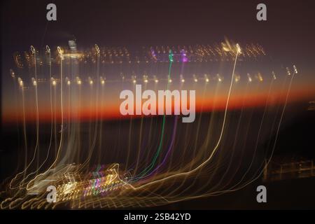 A long exposure shot of cruise ship at night captures swirling abstract light trails against a dark orange sky Stock Photo