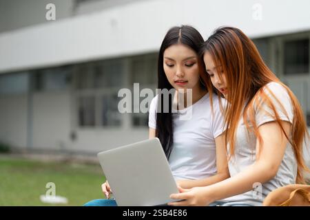 Focused students collaborating on a laptop in an outdoor learning environment Stock Photo