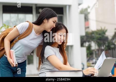 Students collaborating with a laptop and books in an engaging outdoor study session Stock Photo