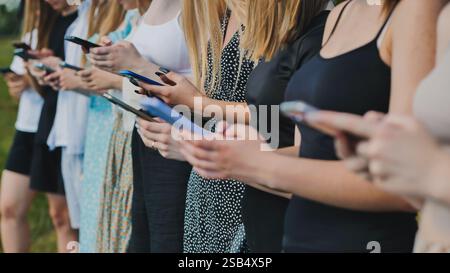Students in a row outdoors, enjoying summer and using their smartphones to browse and connect with friends Stock Photo