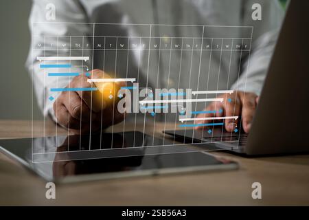 PROJECT MANAGEMENT businessman using a cell phone and laptop to view a project plan Management Software. Scene is focused and professional. Stock Photo