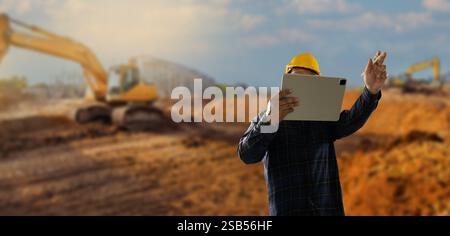 engineer working at site of a large building man wearing a yellow hard hat is looking at a tablet while standing in front of a building. business, Stock Photo