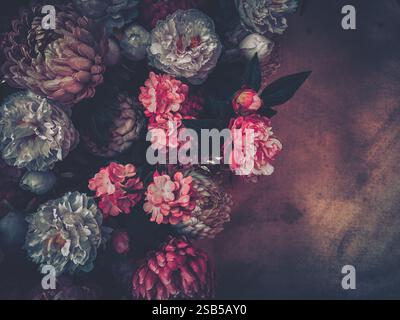 A lush bouquet of pink, grey, and white peonies and other blossoms arranged on a dark, textured background.  The image evokes a vintage, romantic mood Stock Photo