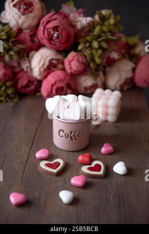 Hot milk with pink marshmallows in mugs with hearts on a wooden background for Valentine's day. Stock Photo