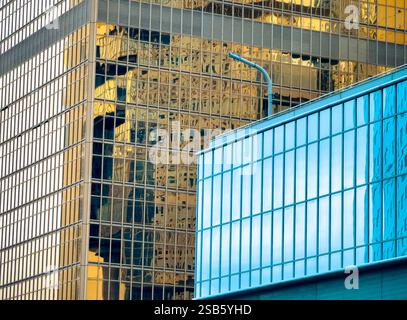Close-up view of modern Hong Kong architecture.  A blue building stands out against a backdrop of gold-toned glass skyscrapers reflecting the city's l Stock Photo