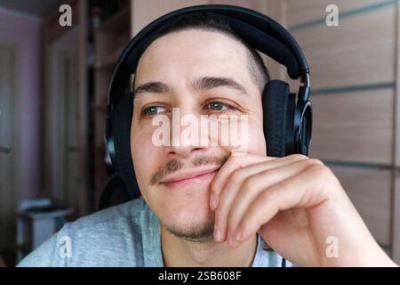 Smiling young man wearing headphones enjoys casual moment at home while engaging in online chat or gaming Stock Photo