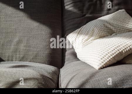 A soft white waffle-textured blanket draped over a grey fabric sofa, creating a cozy and inviting atmosphere. Stock Photo