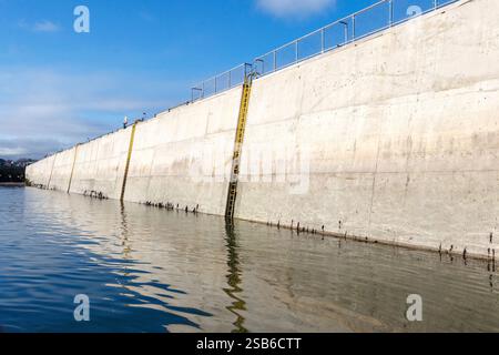 Concrete harbour wall structure with a metal ladder and reflections in calm water on a clear day beadnell harbour northumberland uk Stock Photo