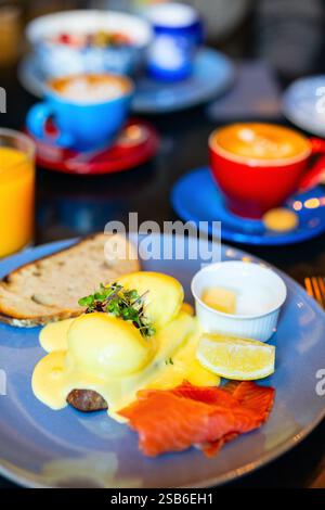 A breakfast plate featuring Eggs Benedict topped with hollandaise sauce, served with smoked salmon, lemon wedge, butter, and sourdough bread Stock Photo