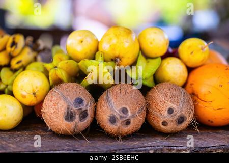 Close-up view of various tropical fruits, including coconuts, star fruit, and bananas, arranged on a wooden surface with a blurred background Stock Photo