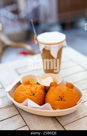 Two bear-shaped salt bread rolls presented on a plate with honey and butter, accompanied by a coffee in paper-cup Stock Photo