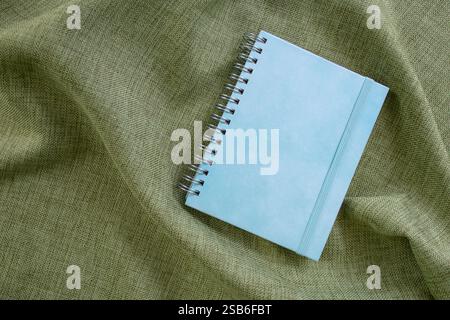Empty blue hard cover notebook   on olive green fabric backdrop, copy space for text Stock Photo