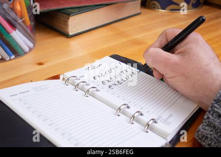 Male hand writing Execute! word on a note book diary, working with a business plan concept, wooden desk Stock Photo