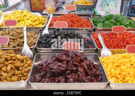 vibrant assortment of Thai candied fruits displayed in stainless steel trays at a local market. This colorful selection includes preserved and candied Stock Photo