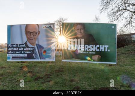 Wahlplakate von CDU und Grünen im Gegenlicht 01.02.25, Hünfelden: Symbolfoto, Illustrationsbild, Symbolbild, Illustrationsfoto, Alltagsszene Wahlplakate von CDU und Grünen im Gegenlicht Zwei Wahlplakate stehen nebeneinander auf einer Wiese im Abendlicht. Links ist ein Plakat der CDU mit Friedrich Merz und dem Slogan Für ein Land, auf das wir wieder stolz sein können. Rechts befindet sich ein Plakat der Grünen mit Robert Habeck und dem Wort ZUVERSICHT. Die tief stehende Sonne scheint direkt zwischen den Plakaten hindurch und erzeugt eine starke Lichtstimmung mit Sonnenstrahlen. Am 23. Februar 2 Stock Photo