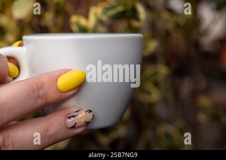 hand with Yellow nail polish for women the handles with the design of the black twigs on camouflage coating. Beautiful manicure with matte yellow coat Stock Photo
