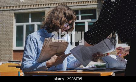 Two high school students collaborate on a project at an outdoor table, exchanging ideas and discussing documents Stock Photo