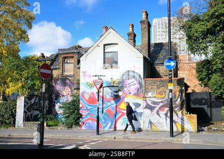 A man walks past a colourful backdrop of street art graffiti on the wall of a building by artists Kaldea and Doudou Style, Croydon, England, UK. Urban Stock Photo