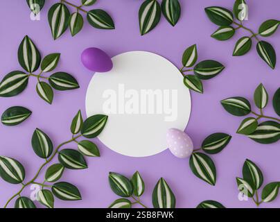 Spring pattern with green and white leaves and purple Easter eggs with paper card note copy space on purple background. Creative Easter concept. Stock Photo