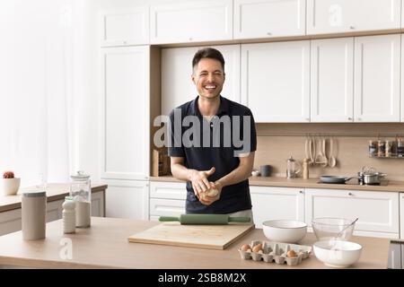 Laughing joyful young man knead dough at modern home kitchen Stock Photo