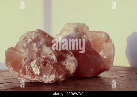 Two large, translucent pink calcite crystals rest on a wooden surface, illuminated by warm light. Stock Photo