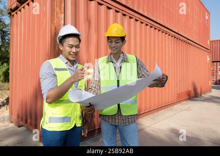 Engineers discussing logistics and reviewing plans at a shipping container facility Stock Photo