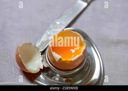 A soft-boiled egg with a rich, golden yolk sits in a polished metal egg cup, its shell delicately cracked open. Stock Photo