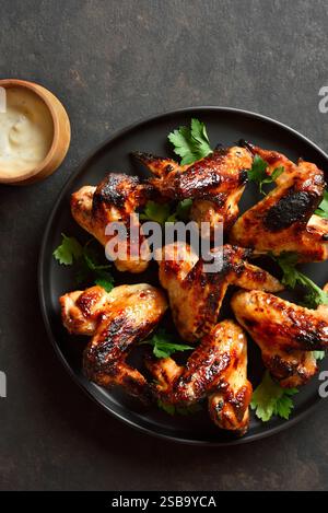 Bbq chicken wings on black plate over dark stone background.  Top view, flat lay Stock Photo