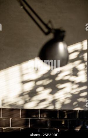 A close-up of a modern black wall lamp casting soft shadows on a textured wall. The interplay of natural light and geometric shapes creates a minimalist and artistic ambiance Stock Photo