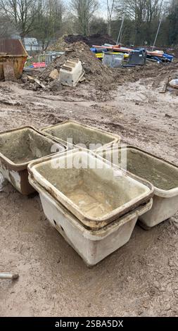 Several stacked, dirty, off-white rectangular plastic containers sit on muddy ground at a construction site.  Construction debris and equipment are vi Stock Photo