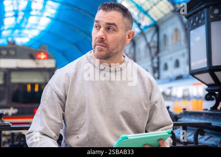Focused Man Using Tablet While Waiting at Train Station looking at camera Stock Photo