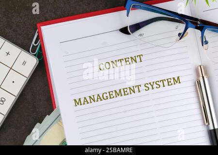 Notebook features a prominent title on content management system alongside glasses and a calculator, highlighting business and technology focus. Stock Photo