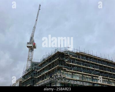 Large Crane Working on a Building Clad in Scaffolding Stock Photo