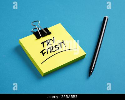 The word try first on yellow sticky note paper with a black pen on blue background. Business product trial offer concept. Stock Photo