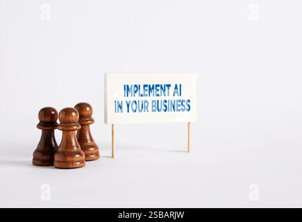 Incorporating Artificial Intelligence into business. Chess pawns standing next to a banner with the message Implement AI in your Business. Stock Photo
