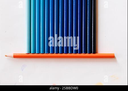 Shades of blue pencils sitting on an orange colored pencil Stock Photo
