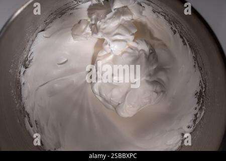 Whipped raw egg white or meringue in a steel bowl of a stand mixer. Place for text. Background with the texture of whipped protein with sugar. Close-u Stock Photo