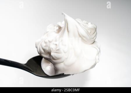 Egg whites or meringues whipped with sugar on a black spoon on a white background. Close-up. Space for text. High quality photo Stock Photo