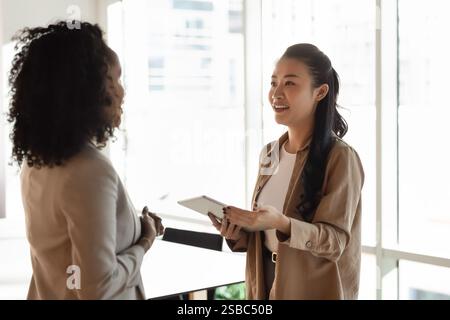 Positive young Asian employee woman asking colleague for advice Stock Photo