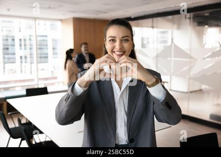 Happy beautiful young businesswoman making hand heart shaped gesture Stock Photo