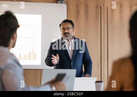 Serious confident mature Indian business teacher giving seminar to students Stock Photo