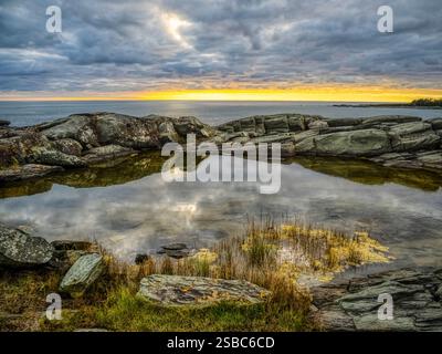 Sunset sky reflecting in a pool of water amoung the rocks at the Cape Forchu Lighthouse on the southwest coast of Nova Scotia Canada Stock Photo