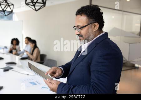 Focused mature Indian business leader man using digital tablet Stock Photo