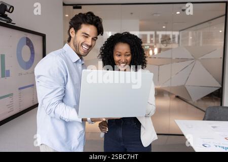 Multiethnic couple of cheerful young colleagues using laptop together Stock Photo