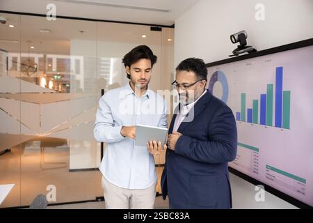 Young Latin employee showing electronic report to elder boss Stock Photo
