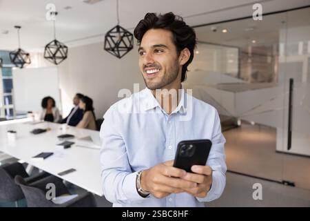 Positive handsome Latin manager man using smartphone in meeting room Stock Photo