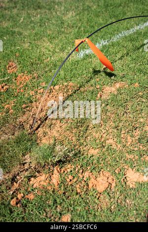 A new fiber optic cable line drop with a warning orange flag tied around it, waiting to be buried underground in the bermuda grass lawn near a house. Stock Photo