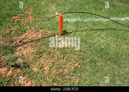 A new fiber optic cable line drop with a warning orange flag tied around it, waiting to be buried underground in the bermuda grass lawn near a house. Stock Photo