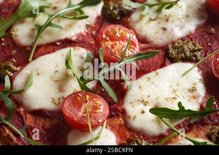 Closeup of homemade gluten-free cauliflower pizza topped with tomatoes, basil pesto, mozzarella and arugula Stock Photo