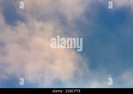 A plane flying away in the evening sky, illuminated by the setting sun. Stock Photo